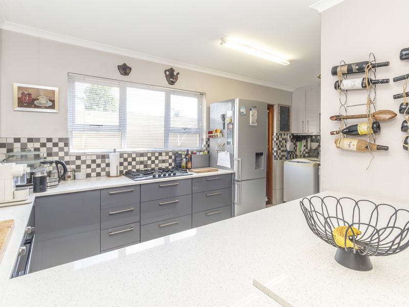 Modern kitchen featuring grey cabinetry, stone countertops, a gas cooktop, and a distinctive checkered tile backsplash, with an adjacent laundry area visible.