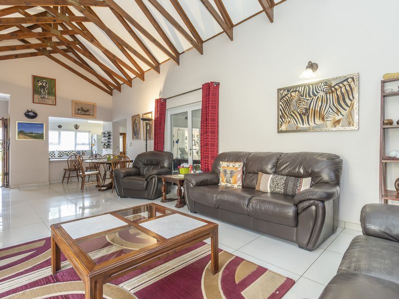 Spacious open-plan living area featuring high vaulted ceilings with exposed timber trusses, tiled flooring, and seamless flow to the dining and kitchen space.