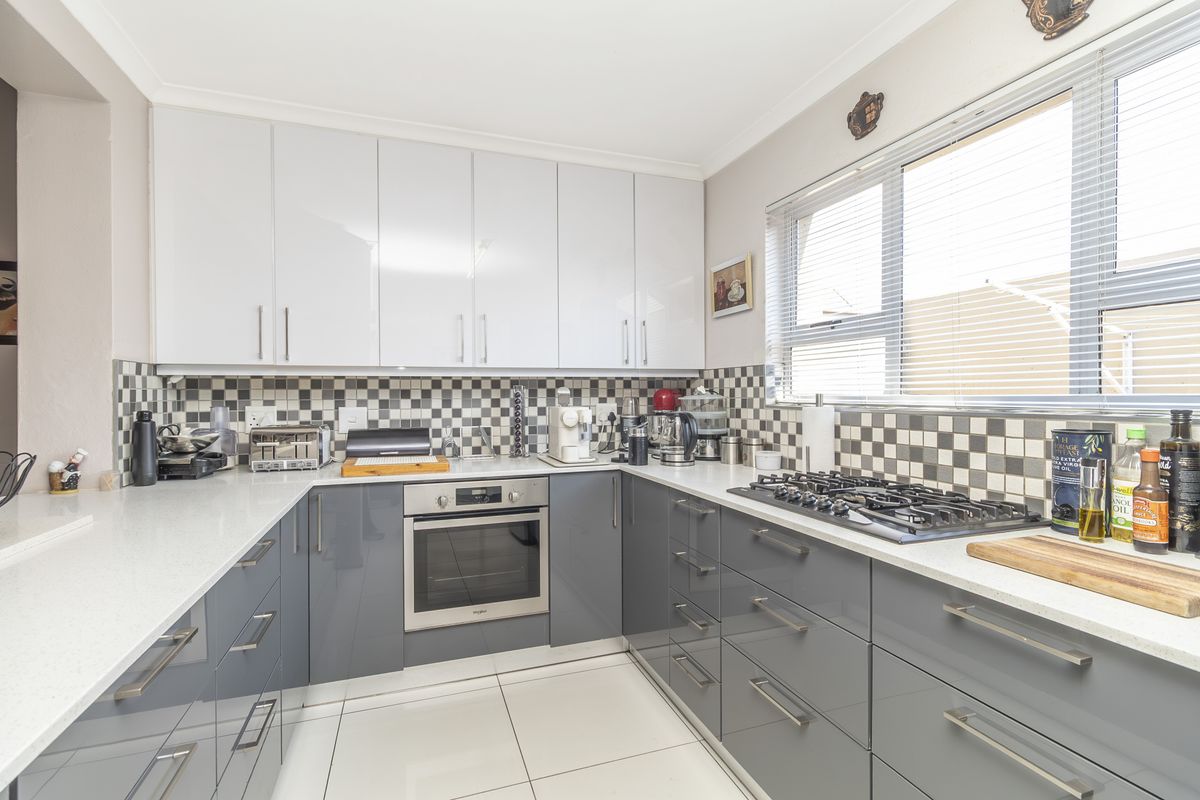 Modern kitchen featuring glossy grey and white cabinetry, white quartz countertops, a gas hob, built-in oven, and a stylish checkered tile backsplash.