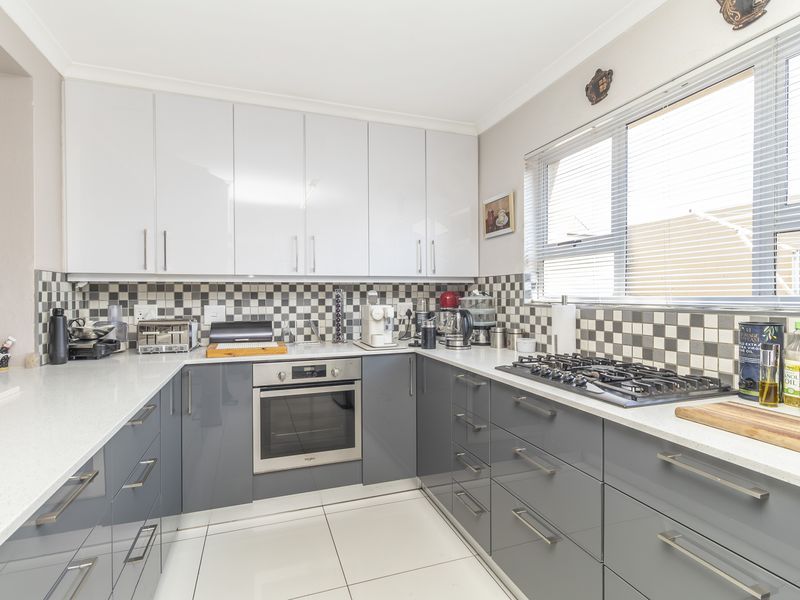 Modern kitchen featuring glossy grey and white cabinetry, white quartz countertops, a gas hob, built-in oven, and a stylish checkered tile backsplash.