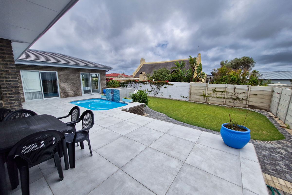Rear exterior view featuring a tiled patio, a small swimming pool with a water feature, and a well-maintained lawn with boundary walling.