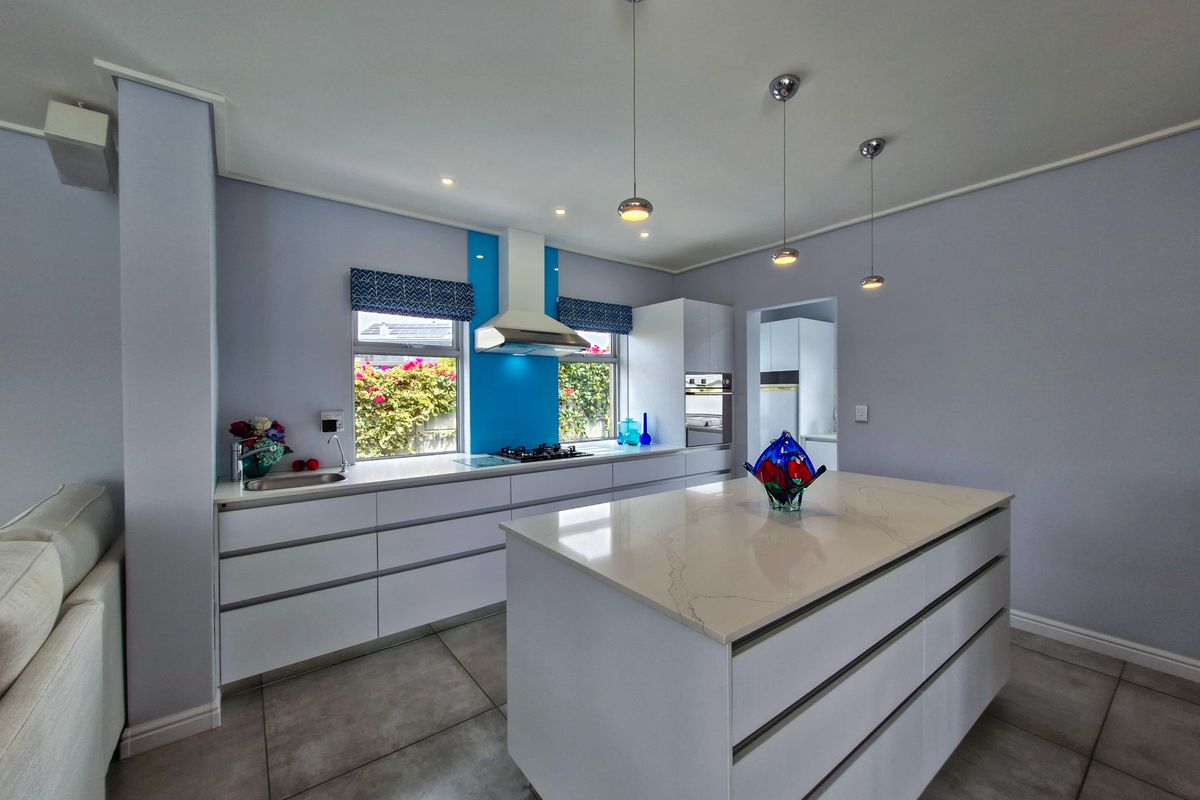 Modern kitchen featuring a central island with stone countertops, built-in appliances, sleek cabinetry, and contemporary pendant lighting.