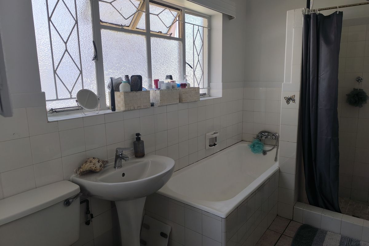 A functional bathroom featuring a pedestal basin, built-in bathtub, and a separate shower enclosure with tiled finishes and a leaded glass window.