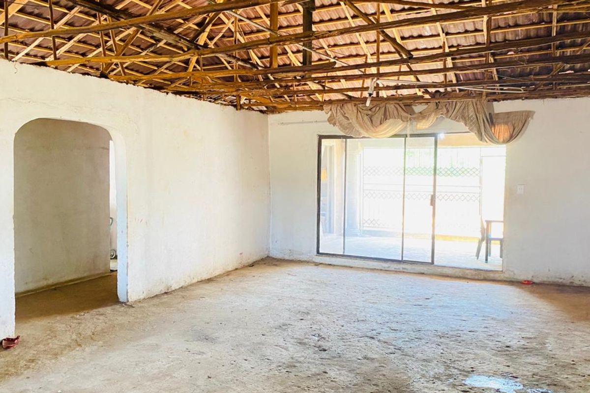 An empty living room space featuring exposed timber roof trusses, an arched doorway, and sliding glass doors leading to an outdoor area.