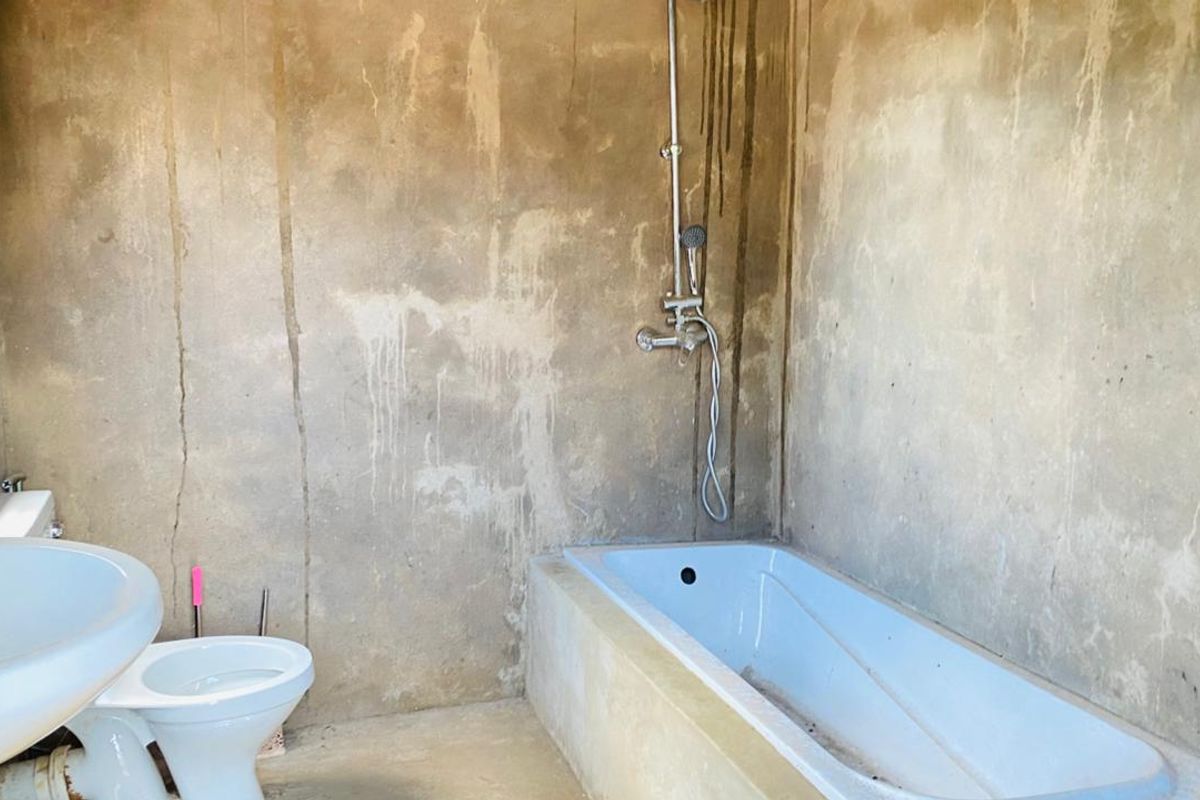 A bathroom in shell condition featuring a built-in bathtub, pedestal basin, and toilet, requiring significant finishing work to the walls and surfaces.