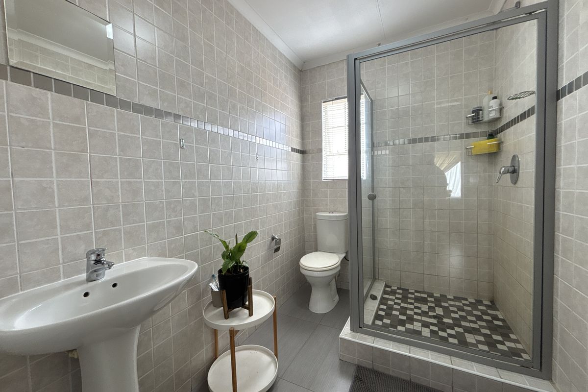 A functional bathroom featuring a pedestal washbasin, a glass-enclosed shower, and neutral wall tiling.
