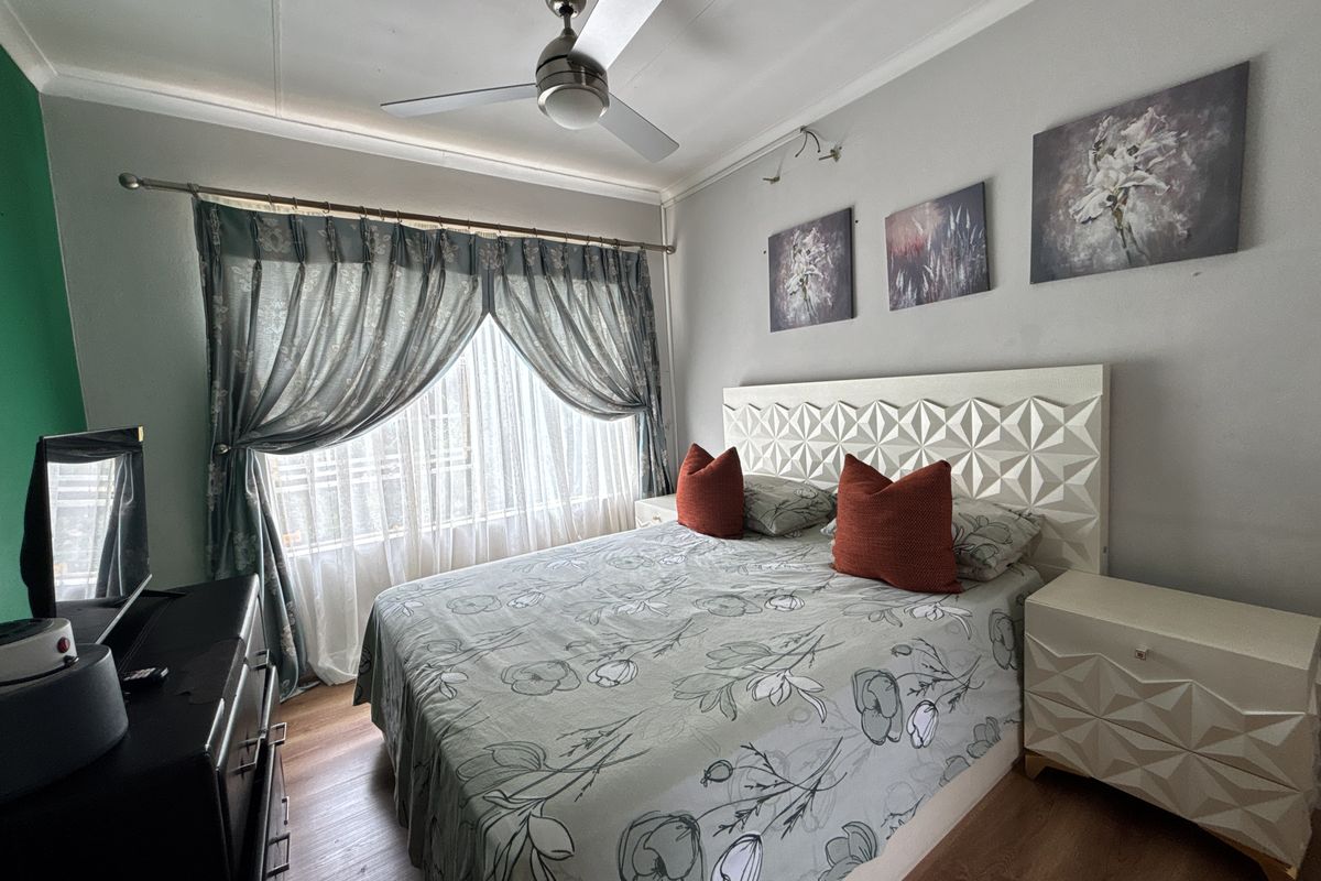 A well-maintained bedroom featuring laminate flooring, a ceiling fan, and a large window with curtain fixtures.