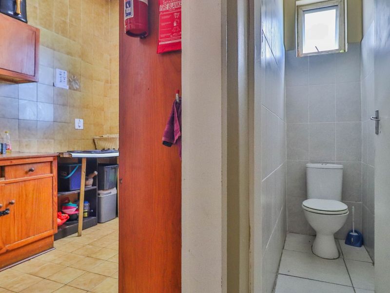 A split view showing a dated kitchen with wooden cabinetry and an adjacent small bathroom with a standard toilet and tiled walls.