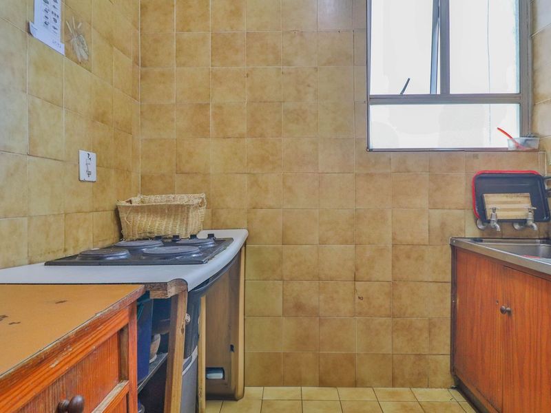 A compact, dated kitchen featuring original cabinetry, a built-in hob, and tiled wall finishes, offering significant potential for a modern renovation.