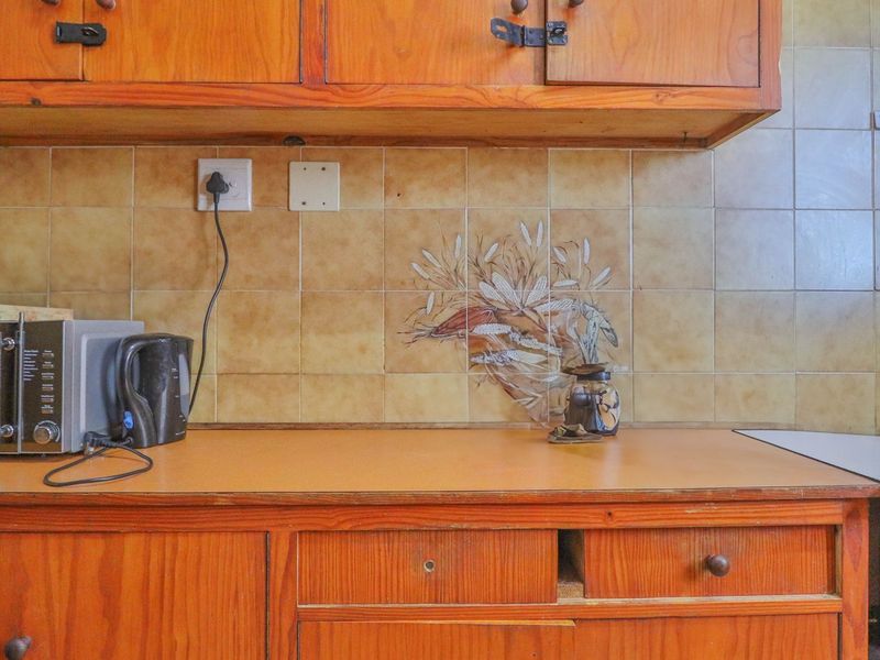 A dated kitchen area featuring wooden cabinetry, a laminate countertop, and a decorative tiled backsplash with integrated electrical outlets.