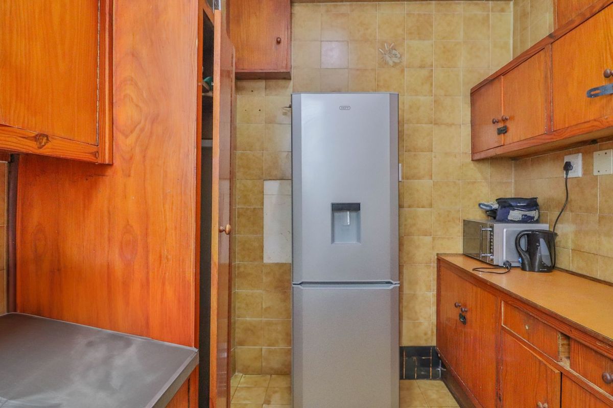 A dated kitchen featuring wooden cabinetry, tiled backsplash, and tiled flooring, offering potential for a modern renovation to update the space.