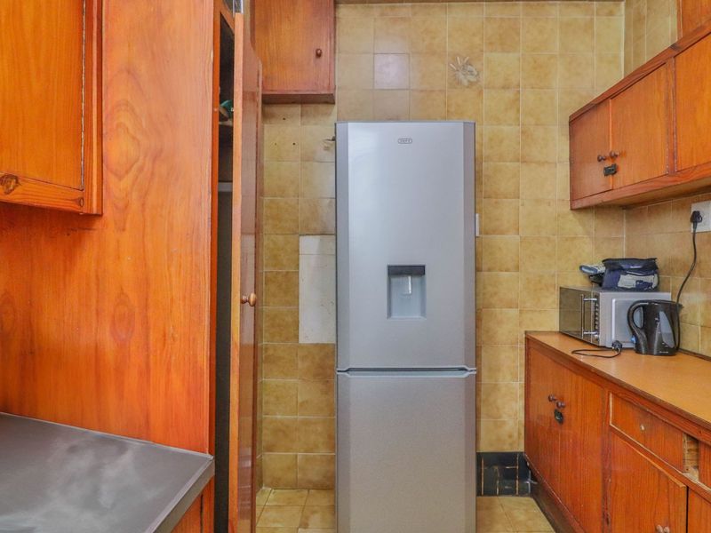 A dated kitchen featuring wooden cabinetry, tiled backsplash, and tiled flooring, offering potential for a modern renovation to update the space.