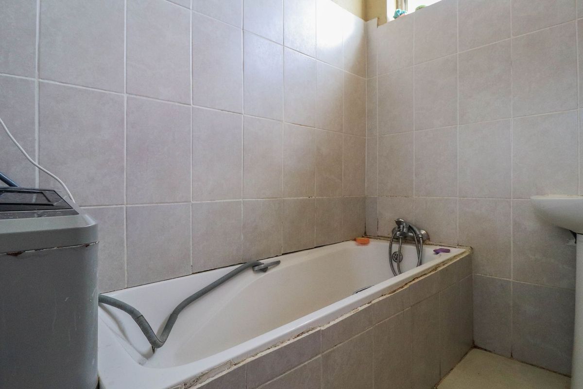 A functional bathroom featuring a bathtub with a mixer tap, a pedestal basin, and neutral ceramic wall tiling throughout.