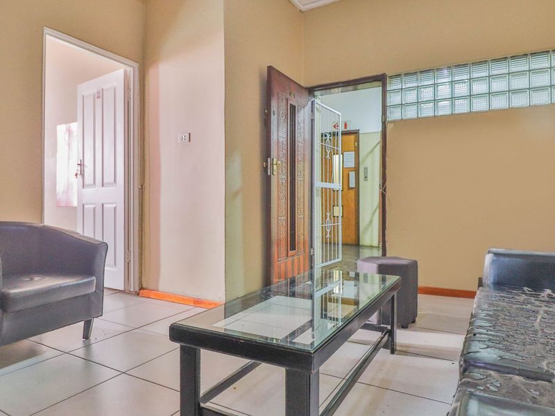 A living room area featuring tiled flooring, a glass block window, and access to an adjacent hallway through a timber door.