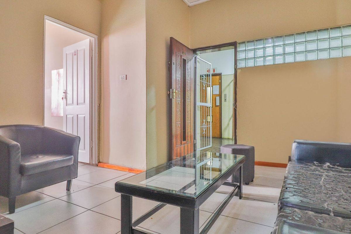A living room area featuring tiled flooring, a glass block window, and access to an adjacent hallway through a timber door.