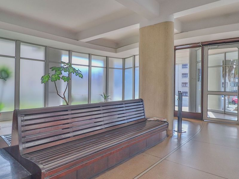 A bright apartment building entrance lobby featuring large frosted glass windows, tiled flooring, and a structural column.