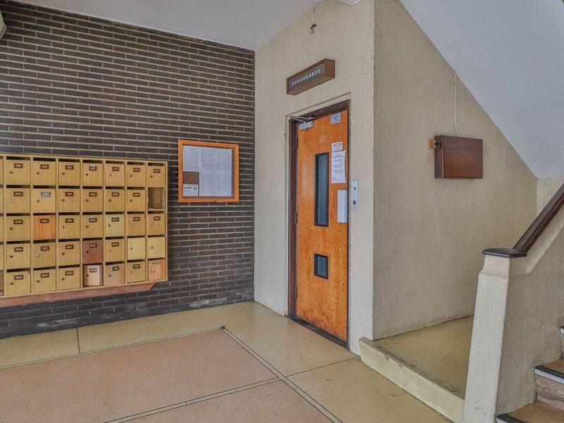 Apartment building entrance lobby featuring a brick wall, built-in mailboxes, elevator access, and a staircase with a handrail.