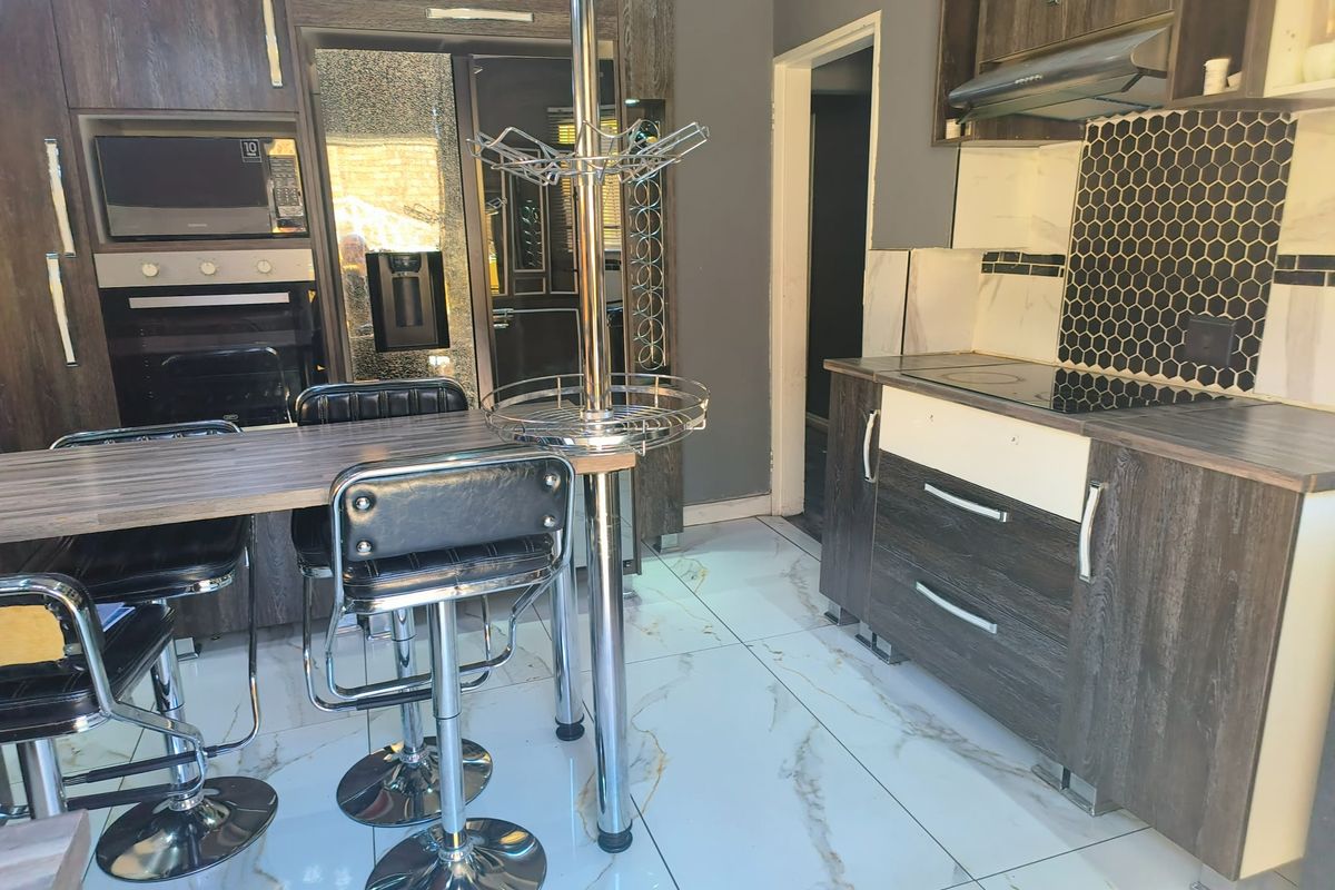 Modern kitchen featuring dark wood-grain cabinetry, integrated oven, built-in microwave, extractor fan, and a breakfast bar with marble-look tiled flooring.