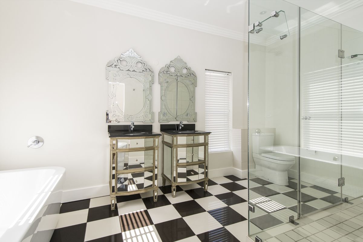 A modern bathroom featuring a glass-enclosed shower, a freestanding bathtub, and dual mirrored vanities with black countertops set against a classic checkered floor.