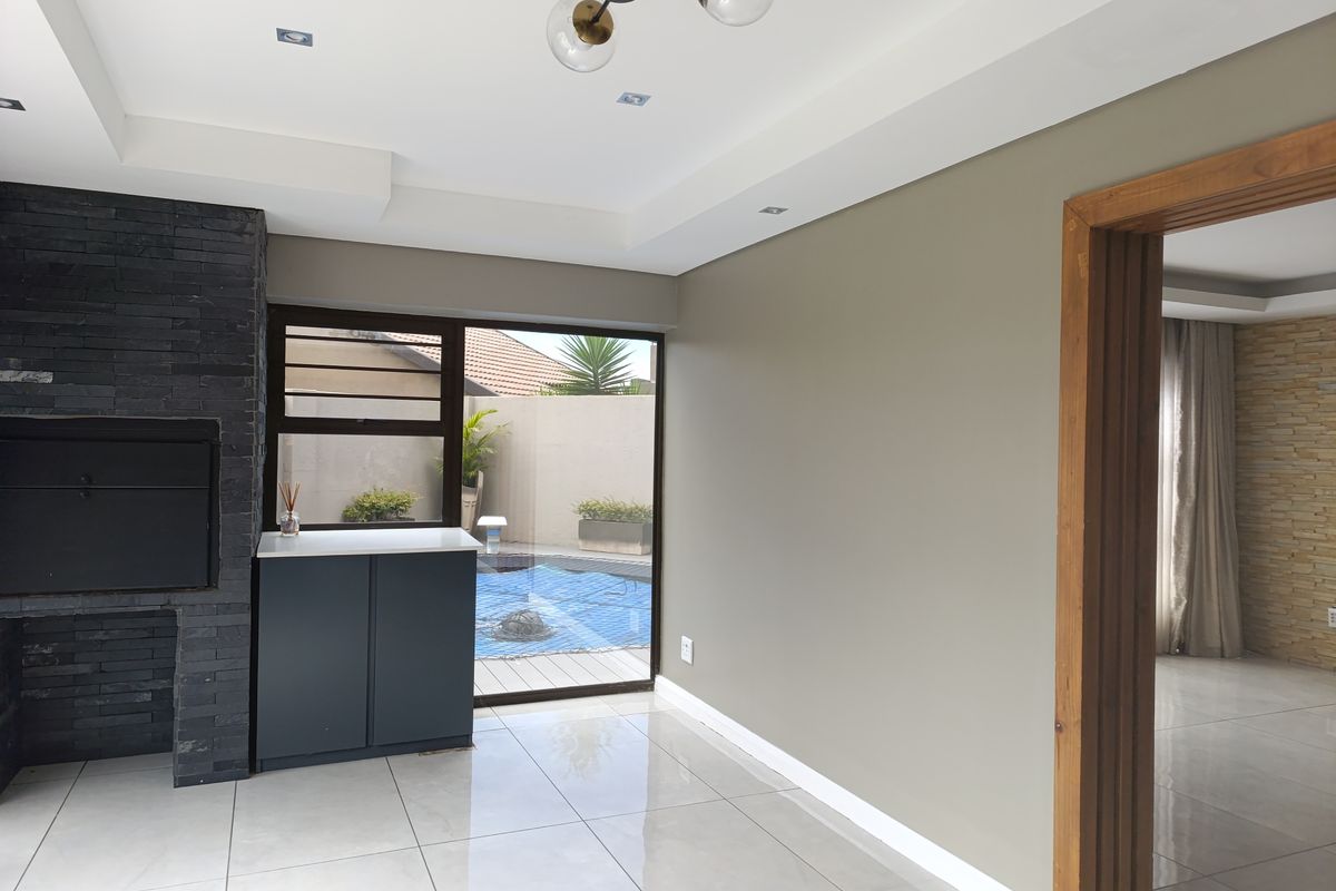 A bright, modern living area featuring a built-in stone fireplace, tiled flooring, and direct access to the pool area through sliding glass doors.