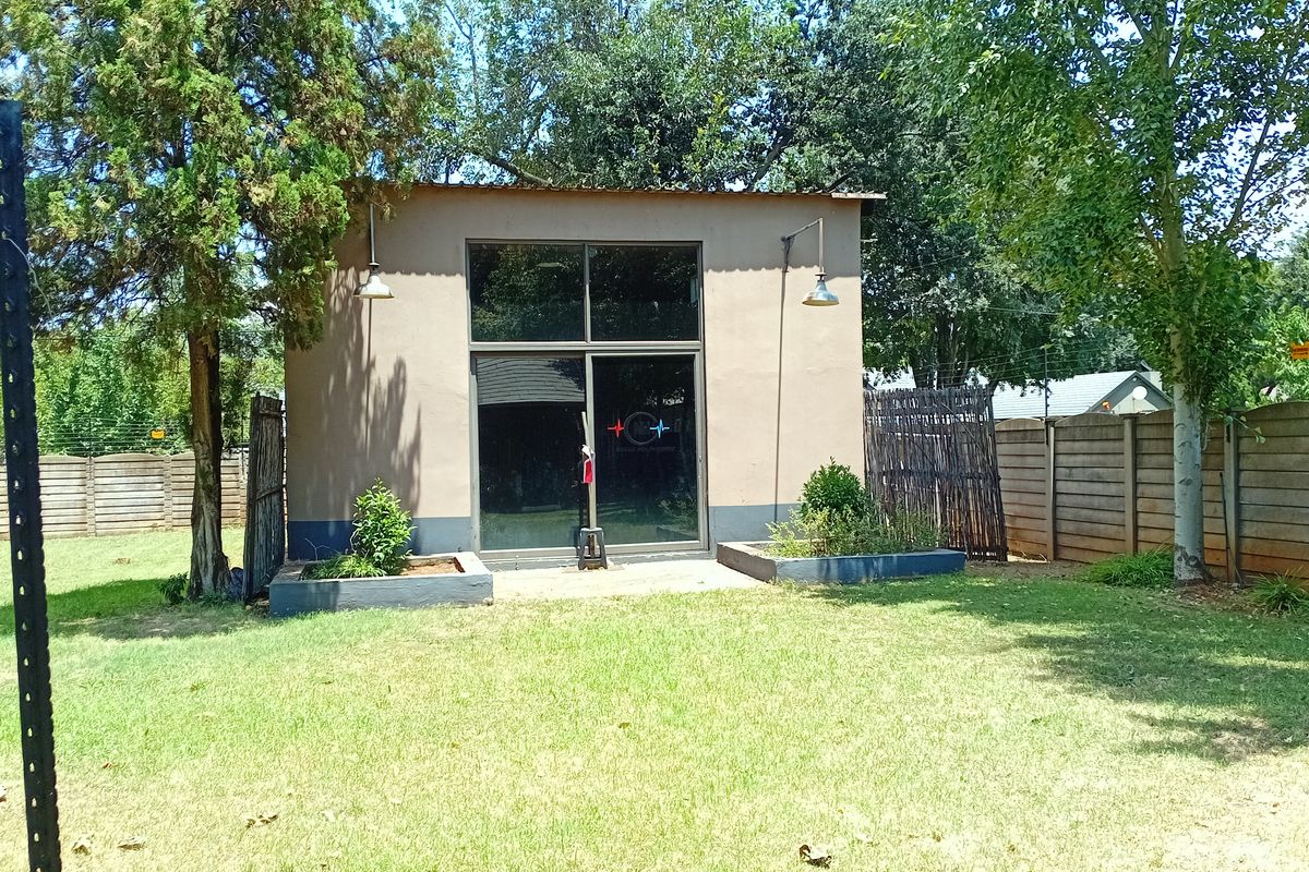 A detached garden studio or utility building featuring large glass sliding doors, exterior wall-mounted lighting, and surrounding landscaped garden area.