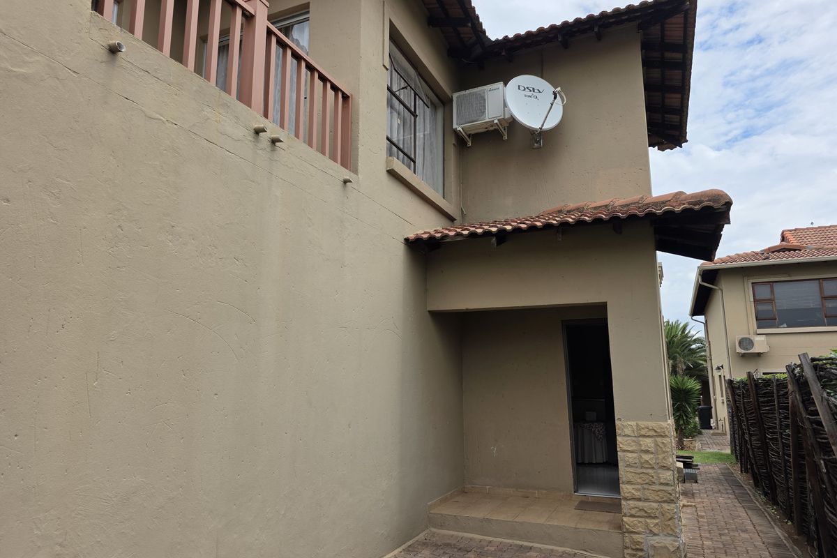 Rear exterior view of the house featuring a paved walkway, stone-clad pillar, balcony, and mounted satellite dish on the rendered wall.