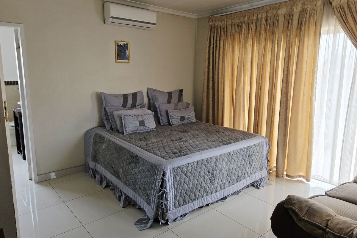 A bedroom featuring tiled flooring, a wall-mounted air conditioning unit, and large sliding glass doors with floor-to-ceiling curtains.