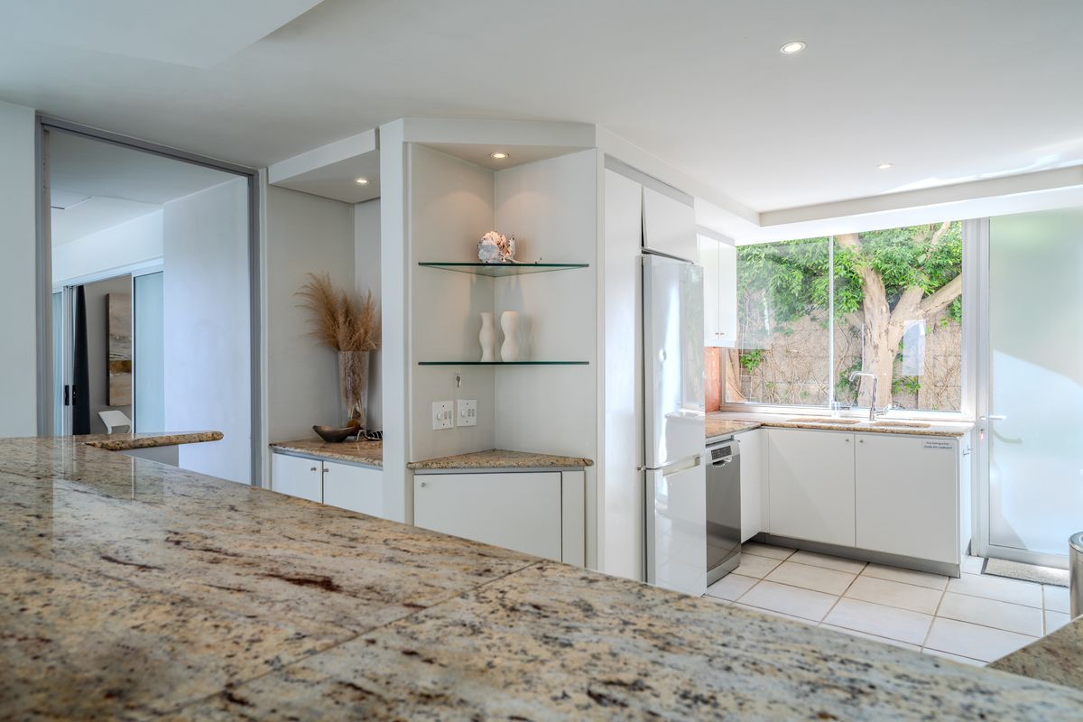 Modern kitchen featuring granite countertops, ample built-in cabinetry, integrated appliances, and large windows overlooking a garden area.