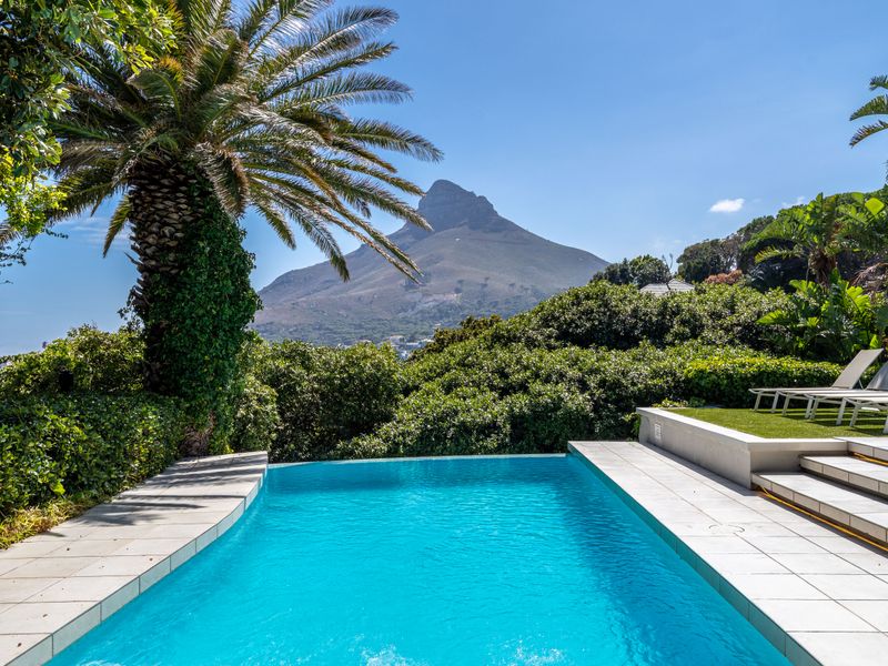 A pristine swimming pool with tiled surround, featuring stunning mountain views and lush garden surroundings.