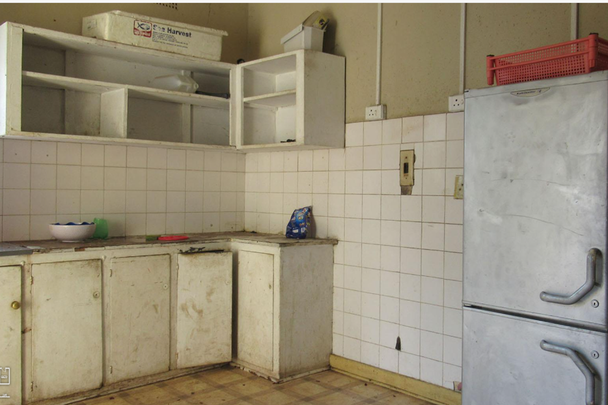 A dated kitchen area featuring original cabinetry, tiled splashbacks, and basic flooring, requiring significant renovation and modernization.