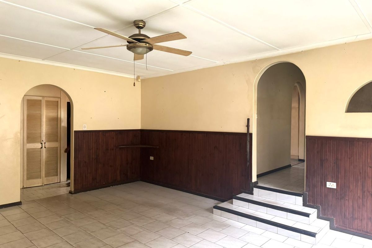 An empty living area featuring timber wall paneling, tiled flooring, and arched architectural details, offering a blank canvas for renovation and modernization.
