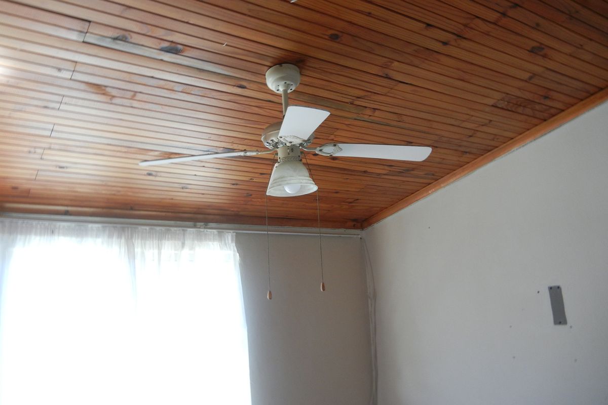 A bedroom space featuring a timber-clad ceiling and a central ceiling fan, currently vacant and requiring minor cosmetic repairs to the walls.