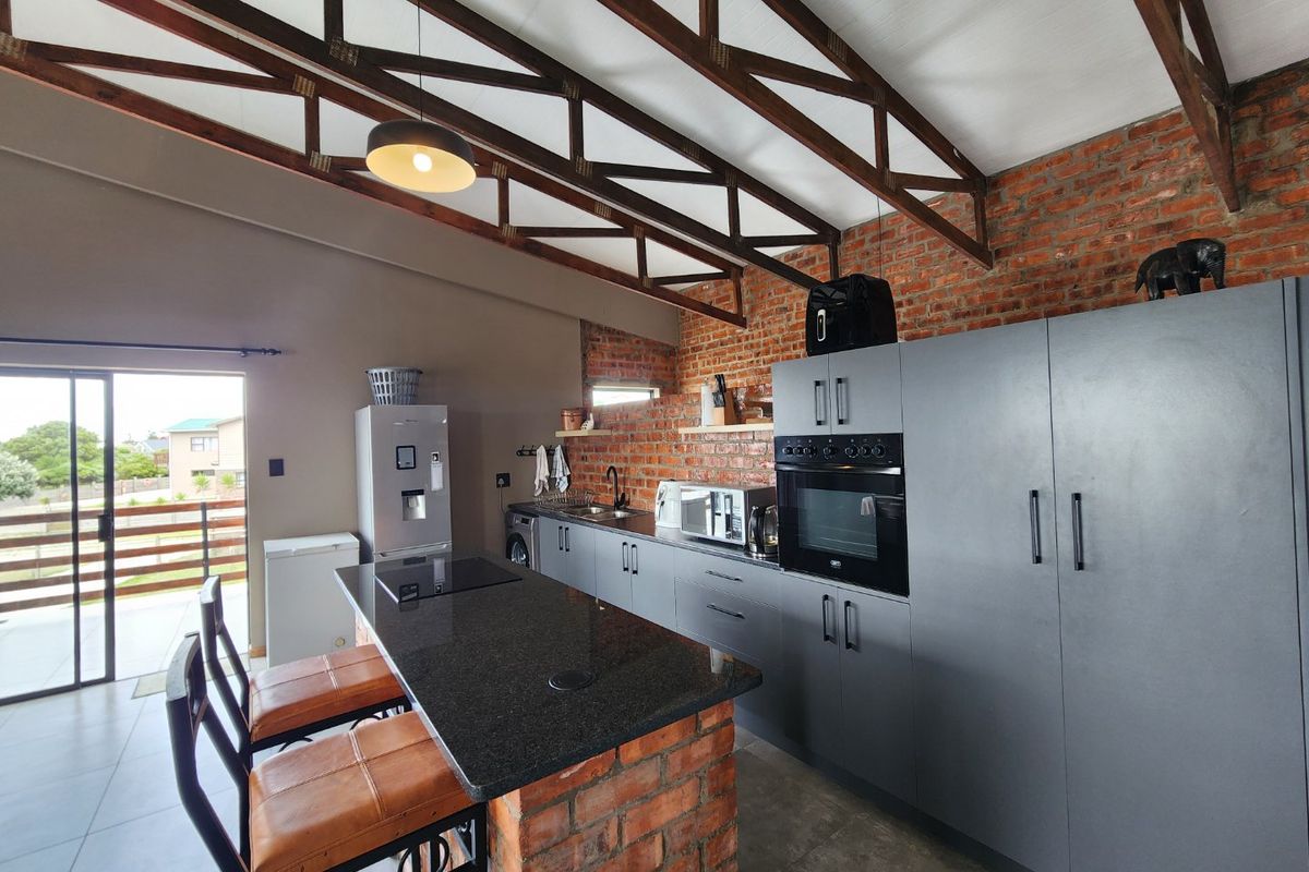 Modern kitchen featuring exposed brick walls, timber roof trusses, granite island, and sleek grey cabinetry with built-in appliances.