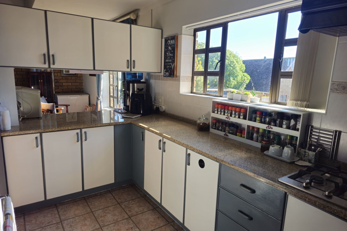 A functional kitchen featuring granite countertops, two-tone cabinetry, a built-in gas hob, and an extractor fan with natural light from the window.