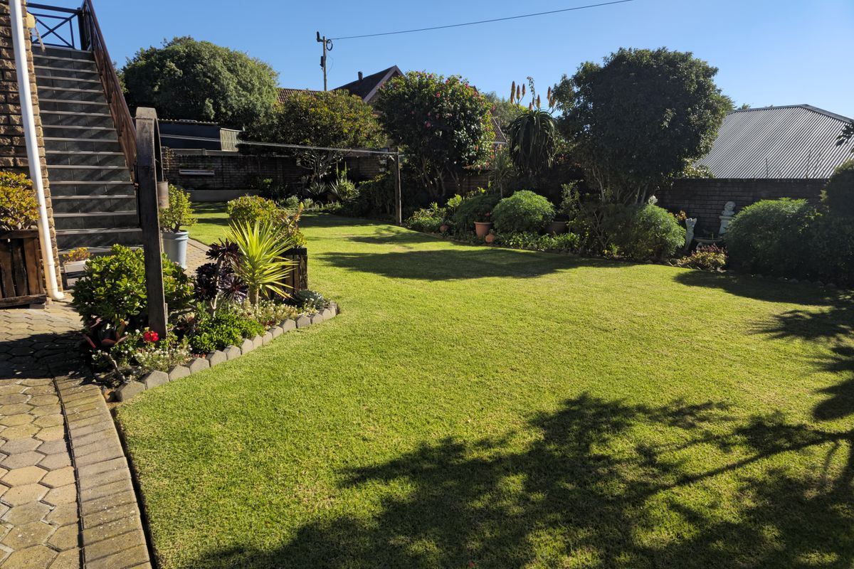 A well-maintained rear garden featuring a lush green lawn, established landscaping, and an external staircase leading to the upper level of the house.