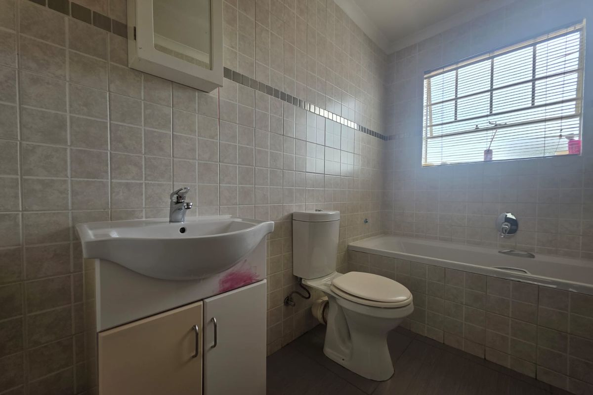 A functional bathroom featuring a tiled finish, a built-in vanity with basin, a standard toilet, and a bathtub with wall-mounted fixtures.