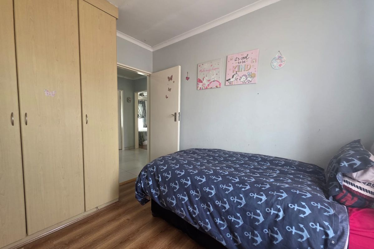 A functional bedroom featuring light wood-finish built-in wardrobes, laminate flooring, and a coved ceiling, providing a practical living space.