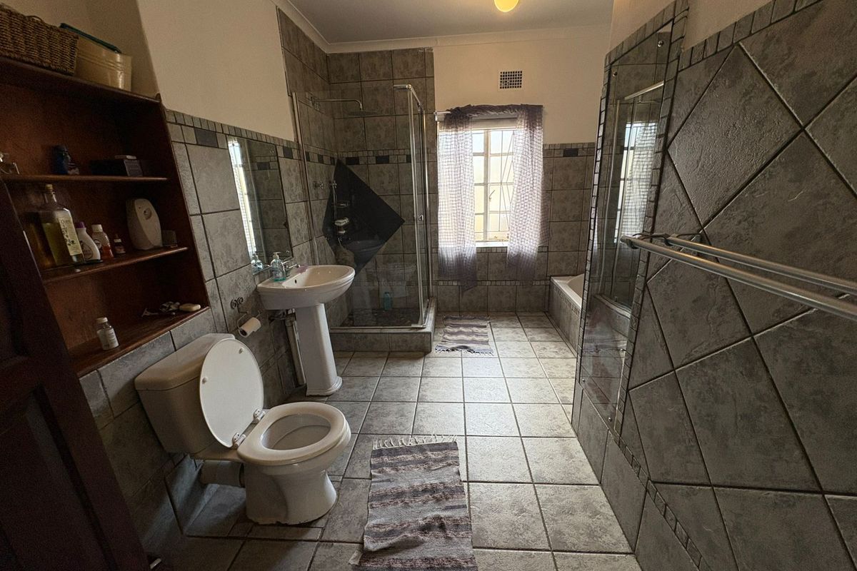 A functional bathroom featuring a pedestal basin, a glass-enclosed shower, a bathtub, and tiled finishes throughout.