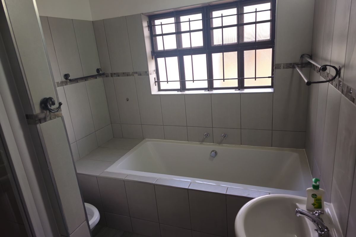 A functional bathroom featuring a built-in bathtub, tiled walls, and a pedestal basin with security bars on the window.