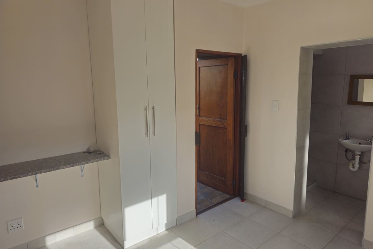 A functional room featuring a built-in white wardrobe, a stone-topped wall-mounted shelf, and an adjacent tiled bathroom area.