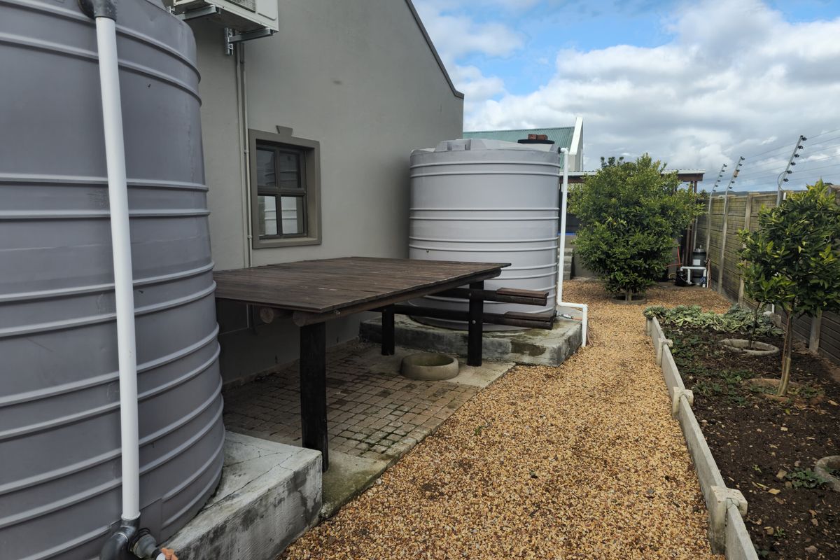 Side exterior area featuring large water storage tanks, a paved section with a wooden structure, and a gravel garden path.