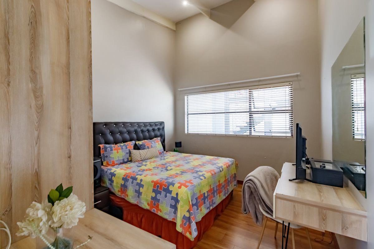 A well-lit bedroom featuring high vaulted ceilings, laminate flooring, and venetian blinds, offering a comfortable and airy living space.