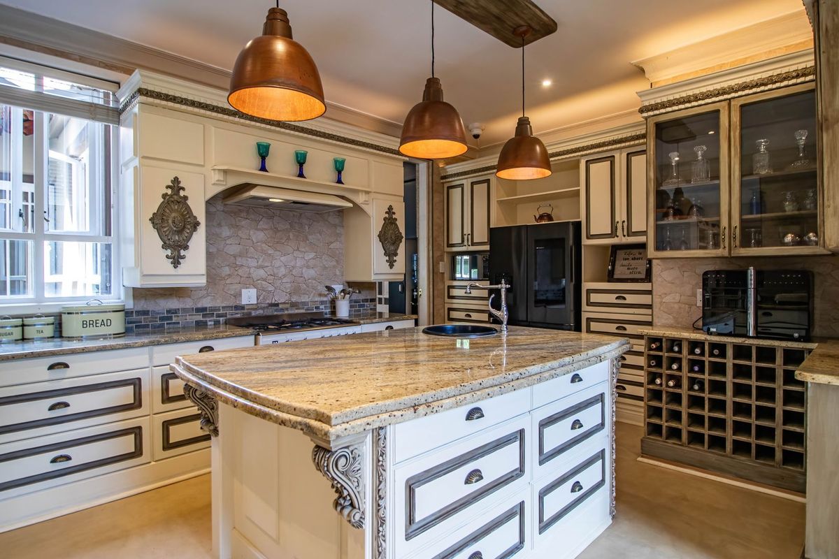 A well-appointed kitchen featuring a large granite-topped island, custom cabinetry, stone backsplash, and elegant pendant lighting, offering a sophisticated and functional culinary space.