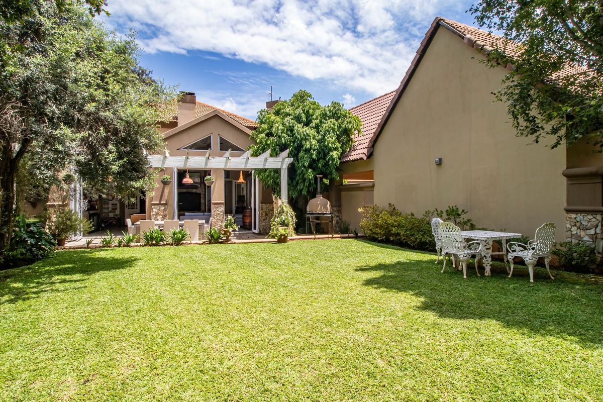 A well-maintained rear garden featuring a paved patio area with a pergola, stone-clad accents, and a built-in pizza oven.
