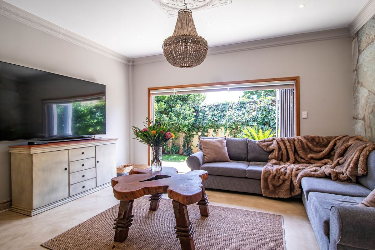 A well-appointed living room featuring a stone accent wall, elegant ceiling rose, and bi-fold doors that open to a private garden.