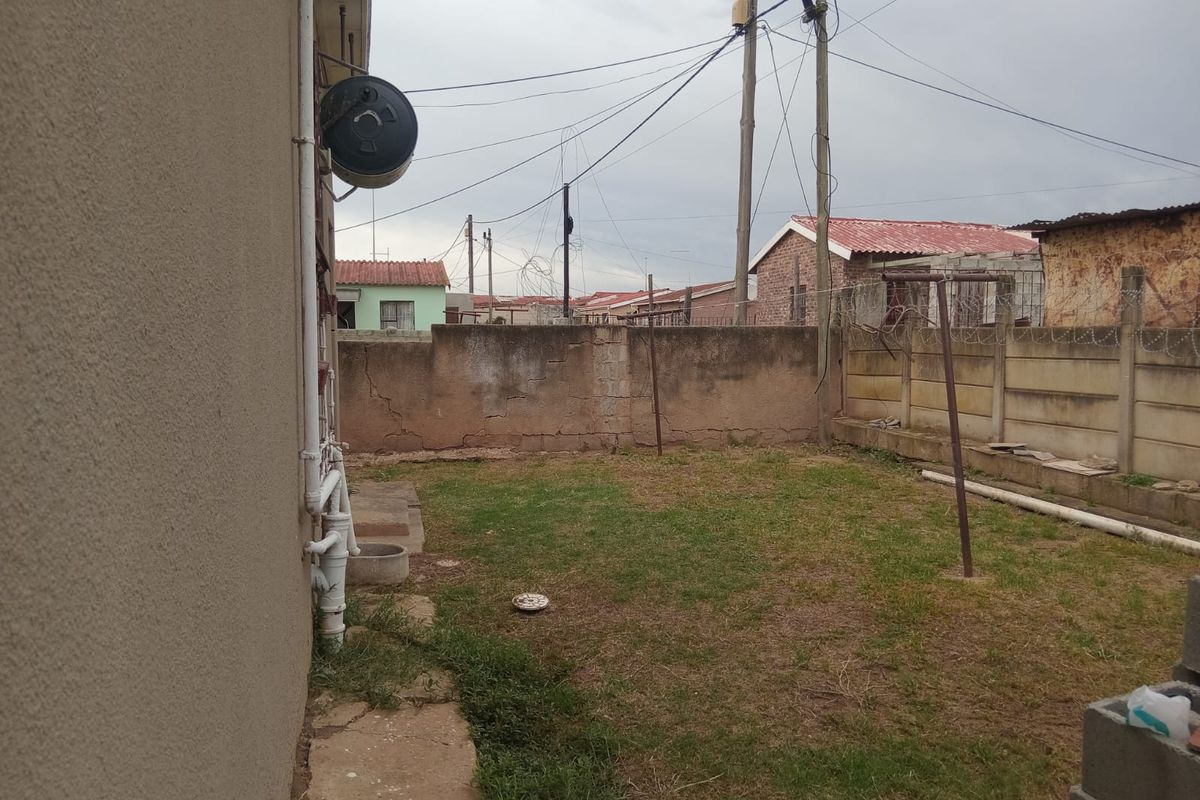 Rear yard area featuring a precast concrete boundary wall with razor wire, an external geyser, and basic lawn space.