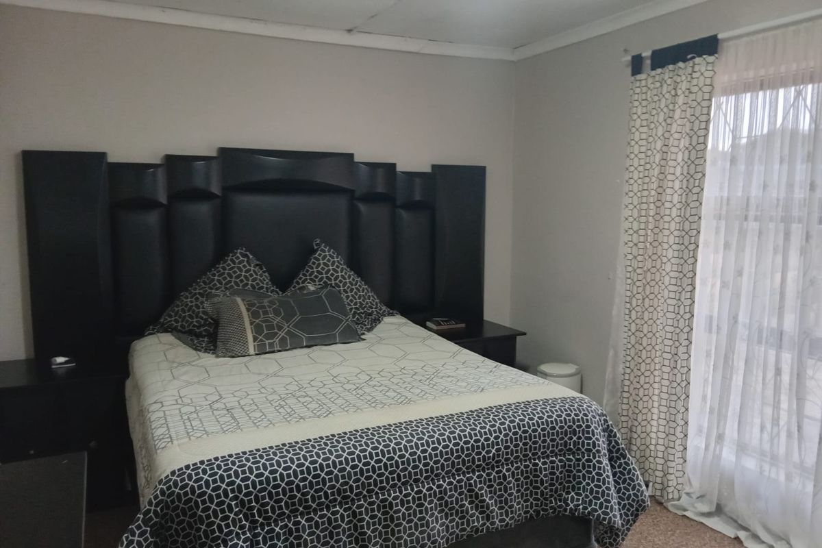 A bedroom featuring a built-in headboard and a window with a security gate. The room requires cosmetic updates to the ceiling and flooring.