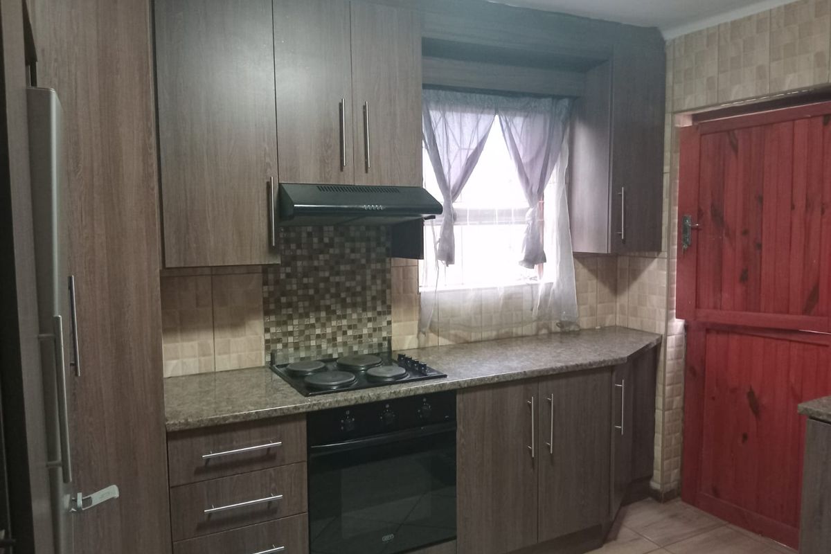 A functional kitchen featuring wood-look cabinetry, a built-in oven with hob, extractor fan, and mosaic tile backsplash.