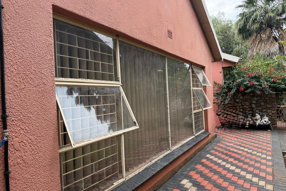 Exterior view of the rear facade featuring large metal-framed windows with security bars and a paved patio area.