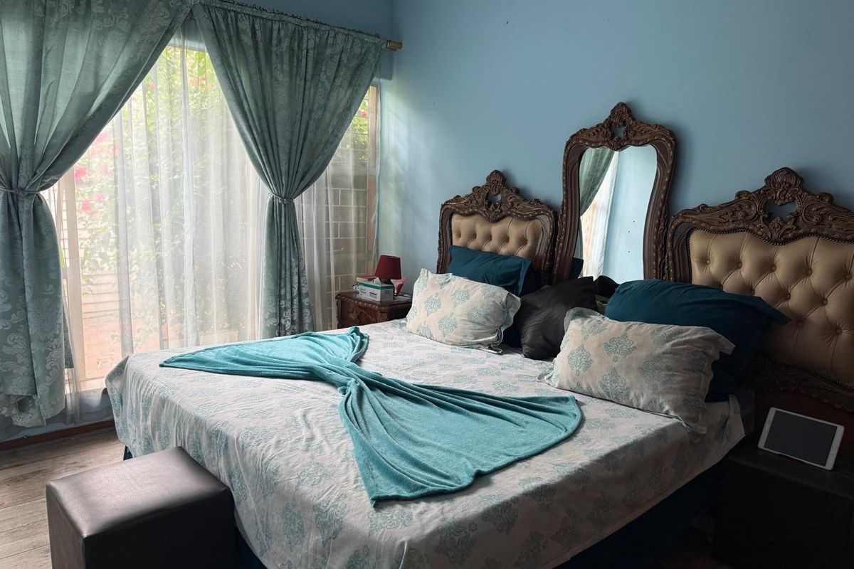 A bedroom featuring light blue walls, large windows with curtains, and tiled flooring.